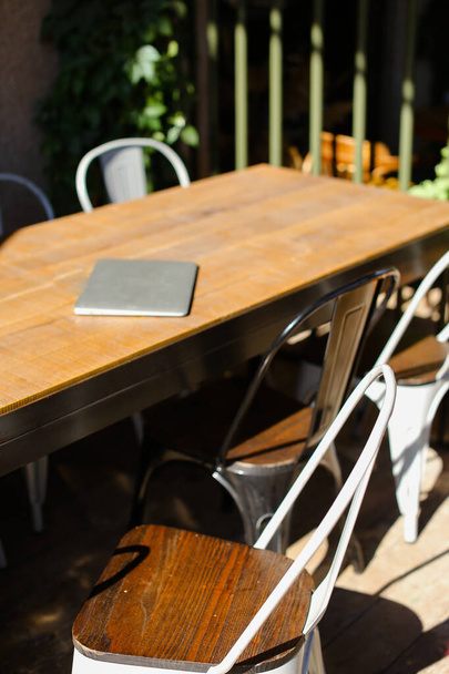 Imagen de la mesa con portátil cerrado y sillas cerca de ella en la cafetería. - Foto, Imagen
