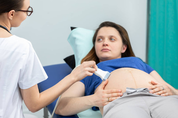 In the gynecology room, a lady doctor examines a pregnant woman using an ultrasound machine. - Foto, imagen