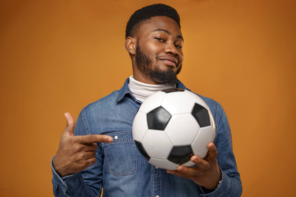 African american man holding soccer ball and pointing on it, yellow background - Φωτογραφία, εικόνα