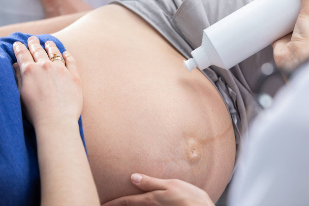 A nurse squeezes gel onto a pregnant patients abdomen and prepares for an ultrasound. Gynecology office. - Fotó, kép