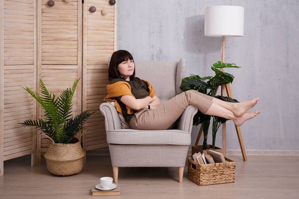 Mujer sentada en un cómodo sillón en una acogedora habitación - Foto, imagen