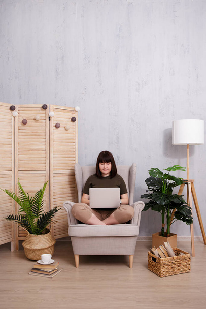 Mujer feliz utilizando el ordenador portátil en acogedora sala de estar con espacio de copia sobre la pared de hormigón - Foto, imagen