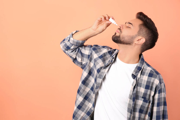 Man using nasal spray on peach background, space for text - Photo, Image