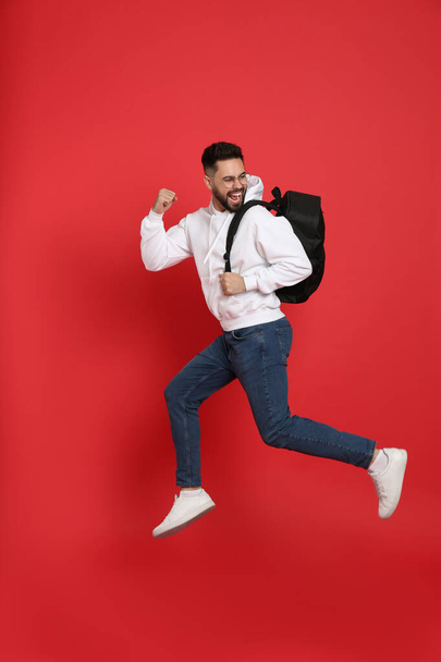 Emotional man with stylish backpack jumping on red background - Foto, immagini