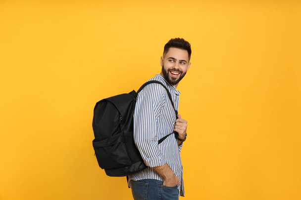 Young man with stylish backpack on yellow background - Фото, зображення