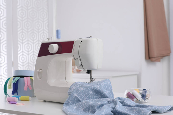 Modern sewing machine, fabric and accessories on table indoors - Valokuva, kuva