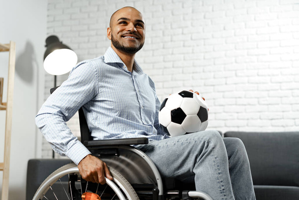 Happy young disabled man in wheelchair holding soccer ball and smiling - Foto, Imagem