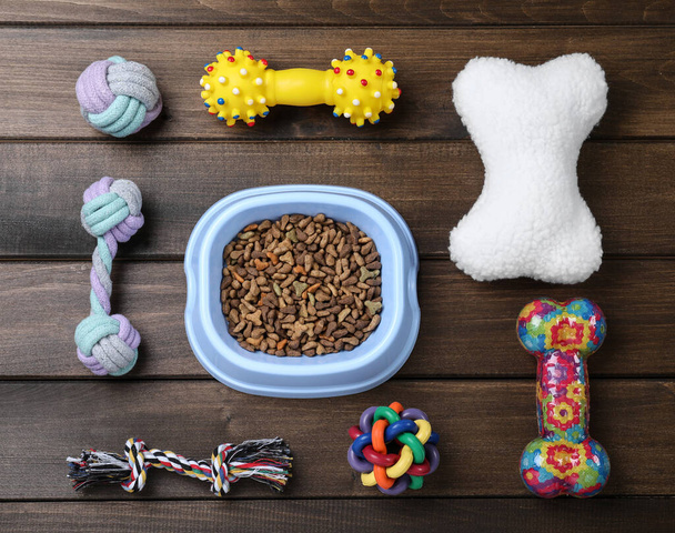 Composición plana con diferentes juguetes para mascotas y tazón de alimentación sobre fondo de madera - Foto, imagen