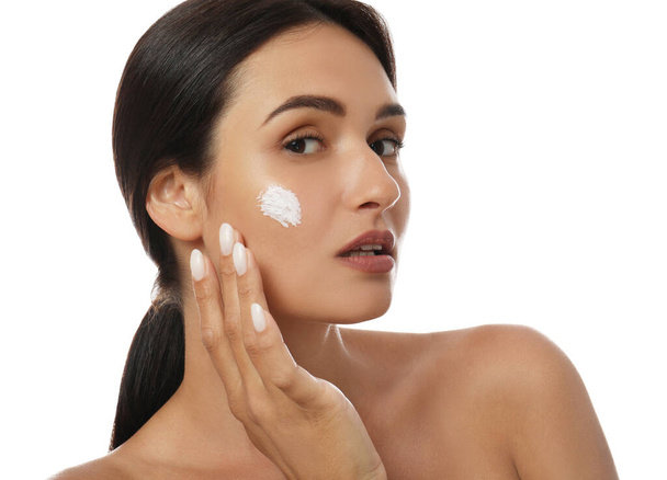 Young woman applying facial cream on white background - Photo, Image