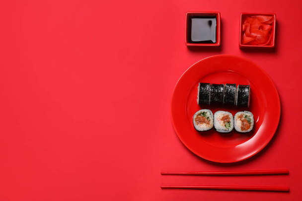 Rolos de sushi saborosos, molho de soja e gengibre no fundo vermelho, flat lay. Espaço para texto - Foto, Imagem