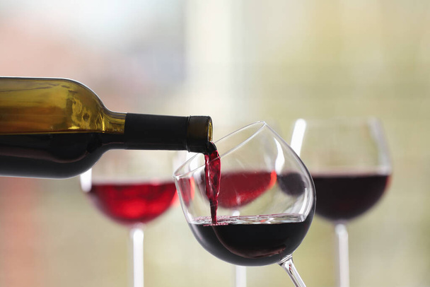 Pouring red wine from bottle into glass on blurred background, closeup - Foto, Bild