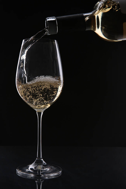 Выливание белого вина из бутылки в бокал на черном фоне - Фото, изображение