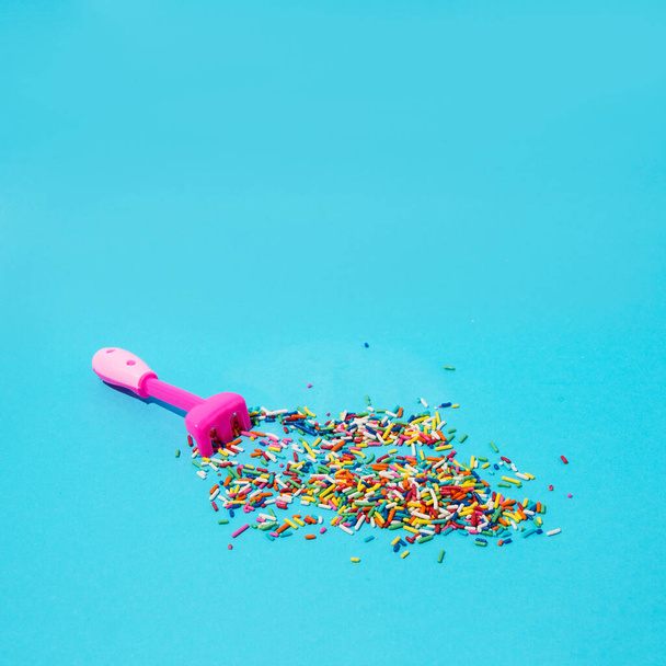 Rastrillo de jardín rosa con pequeños caramelos de colores. Sobre un fondo azul suave. - Foto, Imagen