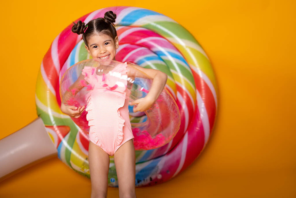 Cute arab little girl in swimming suit and swimming inflatable ring smiling having fun on yellow background - Photo, Image