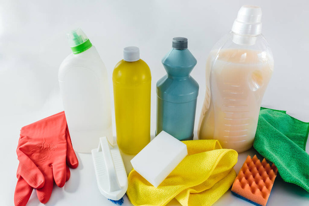 Środki czyszczące - butelki, rękawiczki, gąbki i szmaty na jasnym tle. - Zdjęcie, obraz