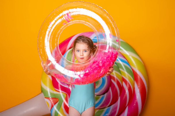 Funny little girl in swimming suit with swimming inflatable ring smiling having fun on yellow background - Foto, afbeelding
