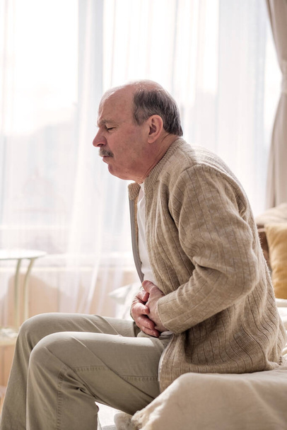 Hombre mayor teniendo dolor de estómago sentado en casa - Foto, imagen