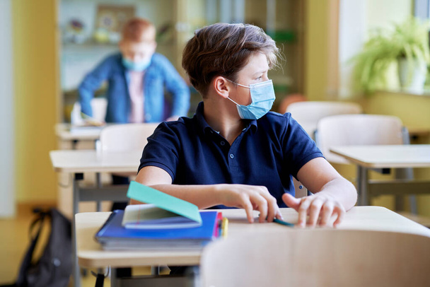 Μαθητής με προστατευτική μάσκα στην τάξη κοιτάζει αλλού. - Φωτογραφία, εικόνα