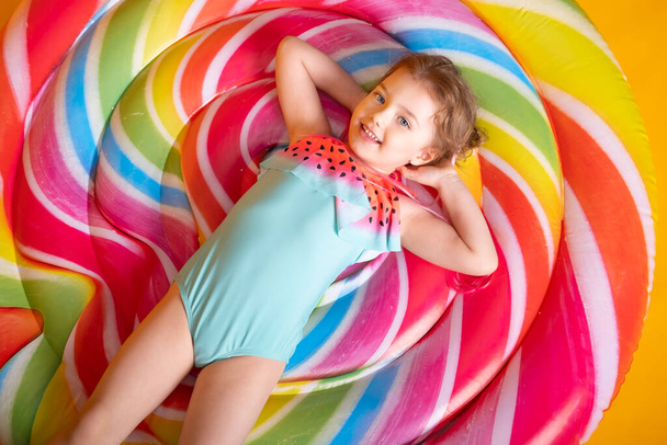 Забавная маленькая девочка в купальнике с надувным кольцом, улыбающаяся, веселящаяся на желтом фоне - Фото, изображение