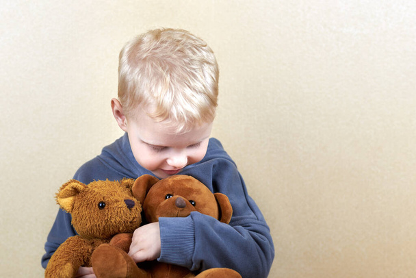 Een driejarige jongen knuffelt twee teddyberen stevig. - Foto, afbeelding
