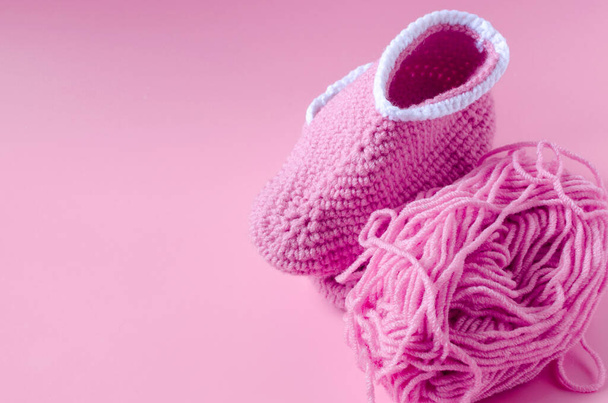 A skein of pink yarn with knitted shoes on a pink kopi space background. Home knitting. - Фото, изображение