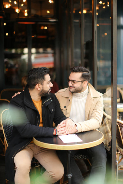 Két európai meleg beszélget a kávézóban és fogja egymás kezét.. - Fotó, kép