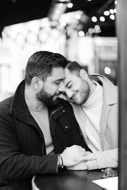 foto in bianco e nero di due gay caucasici seduti e abbracciati, tenendosi per mano. - Foto, immagini