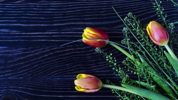 floral arrangement of red and yellow tulips with green leaves on a dark wooden background kopi space - Fotografie, Obrázek