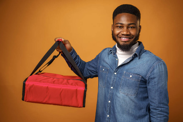 African american courier man holding thermo bag against yellow background - Foto, Bild