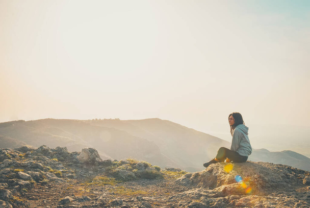Visão traseira imagem de uma mulher sentada sozinha no pico da montanha olhando para a esquerda espaço em branco fundo brilhante - Foto, Imagem