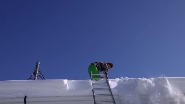 晴れた冬の日に屋根から新鮮な雪を取り除く - 映像、動画