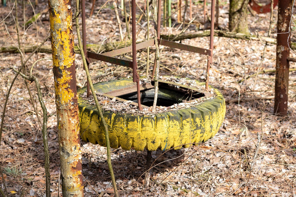 Balanço quebrado velho feito de metal e pneu de carro no playground abandonado entre árvores na cidade fantasma Pripyat, Chernobyl Exclusion Zone, Ucrânia - Foto, Imagem