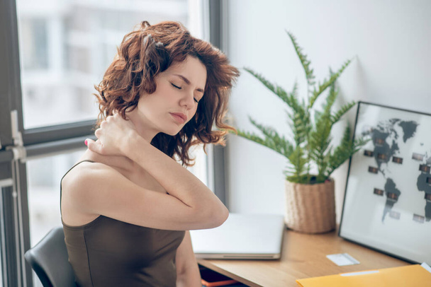 Μια γυναίκα που πονάει το λαιμό της ενώ ξεκουράζεται μετά από μια μέρα σκληρής δουλειάς. - Φωτογραφία, εικόνα