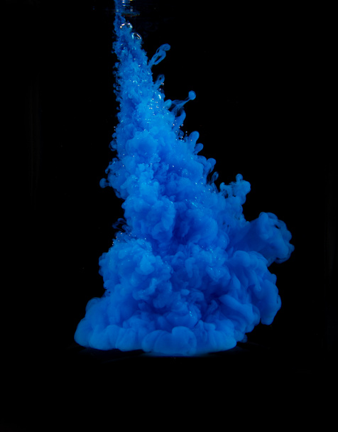ein kräftiger blauer Farbtupfer im Wasser auf schwarzem Hintergrund - Foto, Bild