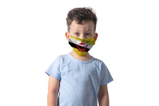 Respirator z flagą Brunei. Biały chłopiec zakłada maskę medyczną na białym tle.. - Zdjęcie, obraz
