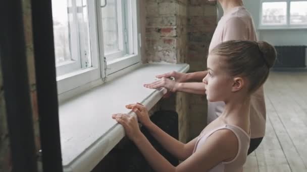 Oldalsó nézet deréktáji felvétel egy keményen dolgozó 9 éves lányról, aki balett órán tornázik női edzővel. - Felvétel, videó