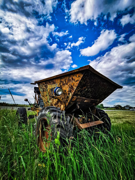 Tractor en un campo verde sobre un fondo cielo nublado - Foto, Imagen