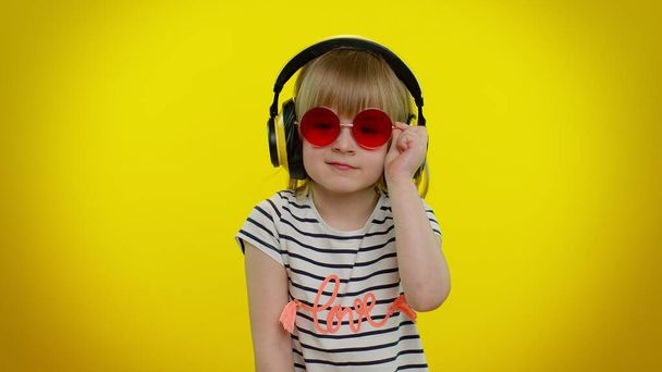 Smiling cute kid child girl in headphones listening music blinking eye, smile, winking, flirting - Foto, Imagen