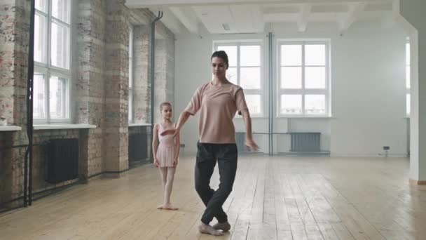 Полный снимок профессиональной балетной тренерши, показывающей изящные балетные движения маленькой девочке, повторяющей их вместе в балетной студии - Кадры, видео