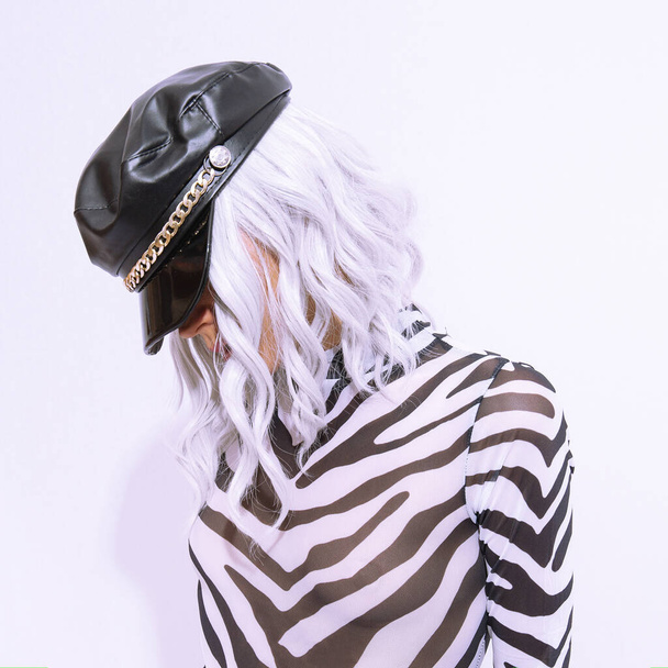 Young  androgenic model in freak stylish zebra print clothes and leather trendy black cap posing in a white studio. Clubbing party style - Photo, image