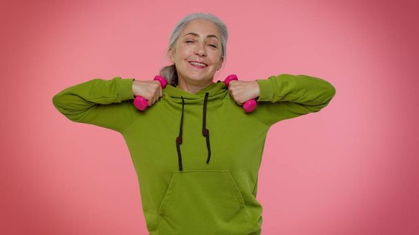 Yaşlı yaşlı kadın spor yapıyor, pembe dambılları kaldırıyor, pilates yapıyor, sağlık hizmeti veriyor. - Fotoğraf, Görsel