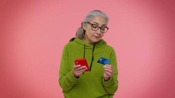 Senior old stylish granny woman using credit bank card and smartphone purchases online shopping - Foto, imagen