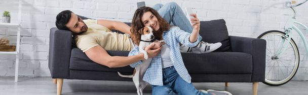 feliz jovem mulher tomando selfie com jack russell terrier e muçulmano namorado, banner - Foto, Imagem