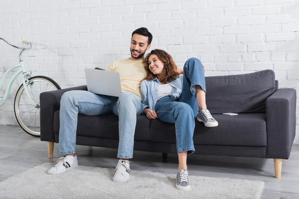 happy interracial couple watching movie on laptop in modern living room  - Foto, Imagem