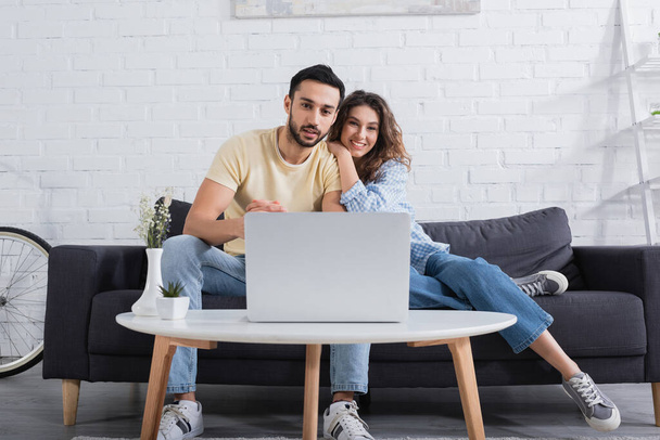 happy interracial couple watching movie on laptop in modern living room  - Fotografie, Obrázek