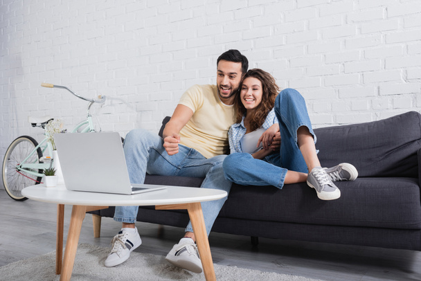 happy muslim man watching movie on laptop with smiling girlfriend  - Photo, Image