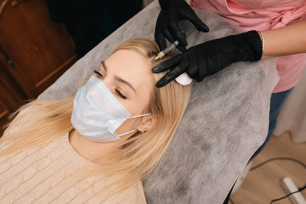 Kosmetikhandschuhe geben der blonden Frau eine Spritze in den Kopf. Mesotherapie, Haarausfall-Therapie. Haarsanierungskonzept. - Foto, Bild
