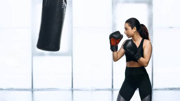 side view of focused woman training with punching bag in gym  - Photo, Image