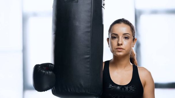 young sportswoman in boxing glove resting near punching bag in gym  - Photo, Image