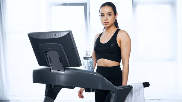 sporty woman in sportswear on treadmill near sports bottle with water in gym - Photo, Image